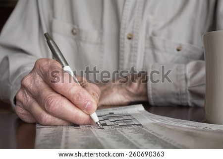 Senior man\'s hand working a crossword puzzle. Shallow depth of field
