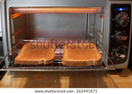 Slices of whole wheat toast on the rack of a toaster oven with open door. Shot from an eye level point of view with shallow depth of field.