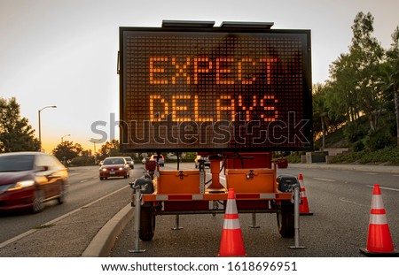Mobile Electronic Traffic Sign stating “expect Delays” taken at sunset with traffic blurred driving past the sign and traffic cones Stock foto © 