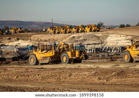 Earth moving equipment at a construction grading site with other tractors lined up in the background