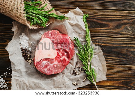 raw meat with salt , rosemary , pepper , spices , sacking and an ax on a wooden background