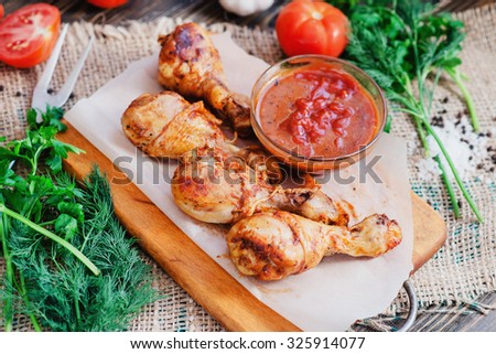 baked chicken legs marinated in garlic with tomatoes , greens , sauce , pepper and salt on a wooden background