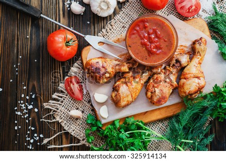 baked chicken legs marinated in garlic with tomatoes , greens , sauce , pepper and salt on a wooden background