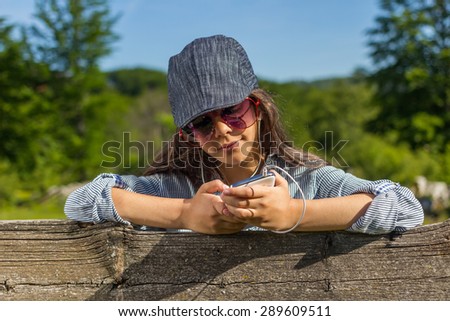 Beautiful young girl with smart phone and headphones listening to music outdoors on sunny spring day.