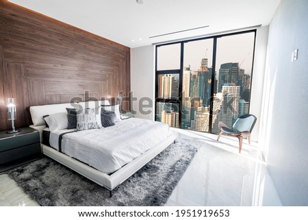 Modern and luxurious bedroom with white ceiling and wood accents with views of Bangkok skyline. Condo or Hotel accomodation.