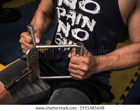 Closeup of an anonymous muscular man doing seated v-bar cable rows at the gym or fitness center. Wearing a No pain No gain tank top. Middle back workout. Stock fotó © 