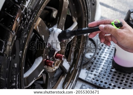 A worker thoroughly cleans the spokes of a wheel's rim with a fine brush. During a full detail and exterior car wash. Stock fotó © 