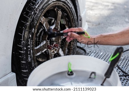 A man use a fine brush to clean the lug nuts and center cap of the rim of a car's front tire. At a carwash or auto detailing shop. Stock fotó © 