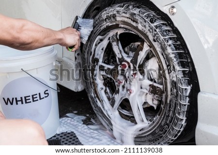 A man use a large brush to scrub clean a car's front tire and loosen dirt and grime in the grooves. At a carwash or auto detailing shop. Stock fotó © 
