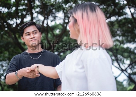 A young man giving a handshake to a young woman he met in the park. A slight smile expressing love, happiness, or luck. Imagine de stoc © 