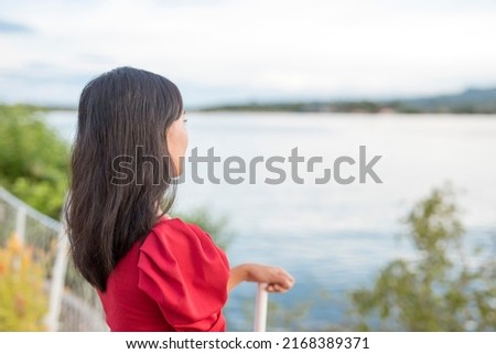 A young woman in a red blouse ponders while looking at the sea view. Getting some fresh air to think clearly. Work or relationship problems. 商業照片 © 