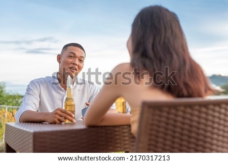A young man converses with a pretty woman he met for the first time. A first date going great so far. Outdoor waterfront bar or cafe location. Imagine de stoc © 