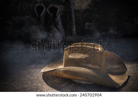 American West rodeo cowboy felt hat and authentic leather western riding boots with vintage ranching gear on weathered wood floor in an old ranch barn