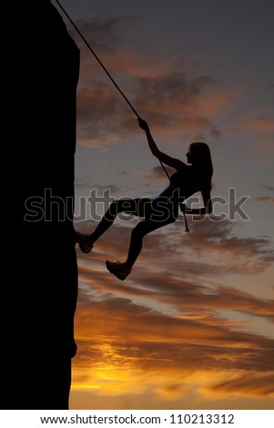 A silhouette of a woman rock climbing with a beautiful sky behind her.