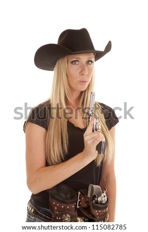 A cowgirl dressed in black holding on to her pistol blowing on the tip of the gun.