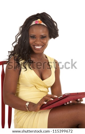 A woman sitting in her red chair in her yellow dress with a smile on her face with her electronic tablet in her hands.