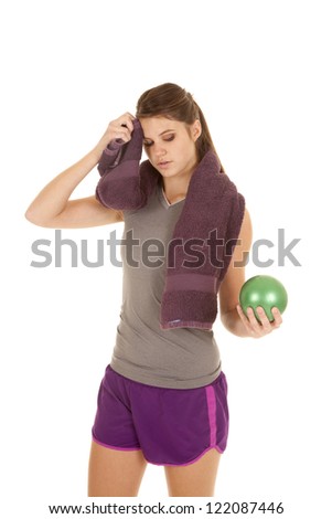 a woman working out with her green weigted ball and wiping her sweat with a towel.