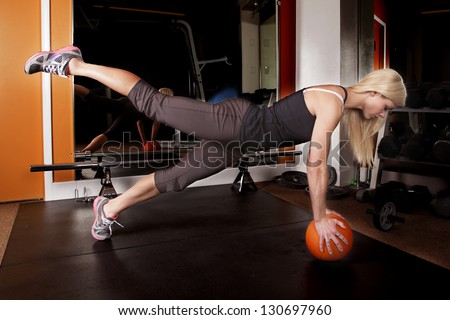 A woman showing off her strength by doing a push up on a ball with one leg up.