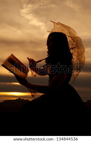 A silhouette of a woman using the last light of day to read a book out in the sunset.