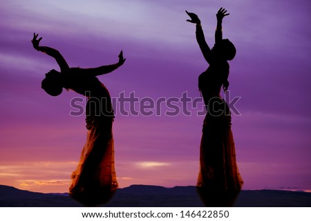A silhouette of two women belly dancing.