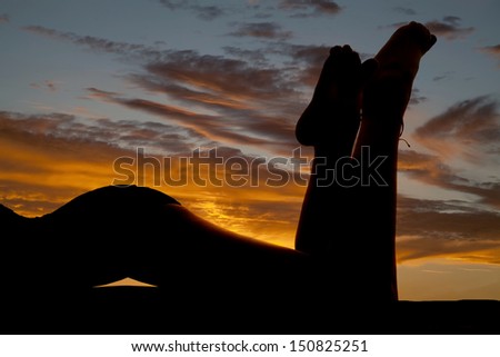 a silhouette of a woman\'s legs laying on a beach with the sunset behind her.