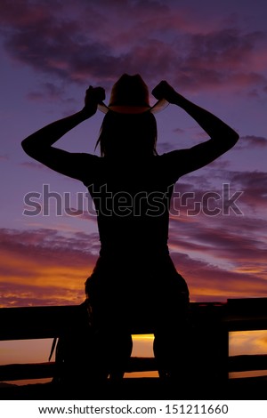 A silhouette of a woman in her western wear holding on to the brim of her hat.