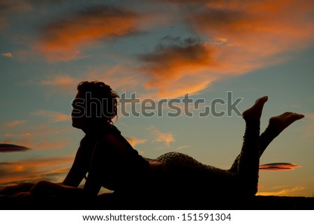 A silhouette of a woman on her belly with her feet up.