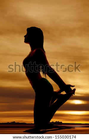 A silhouette of a woman  on her knees holding up her feet.