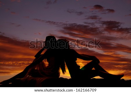 A silhouette of two women sitting with their backs together.