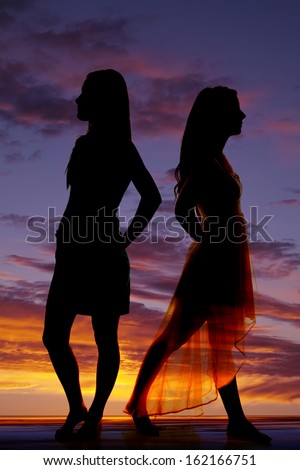 Two women are standing back to back in front of a sky.