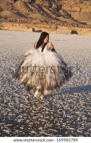 a woman in her formal dress running on the frozen snow patched covered lake.