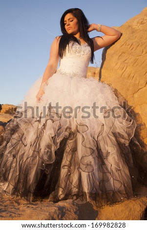 a woman in her formal dress looking down, while standing on rocks.