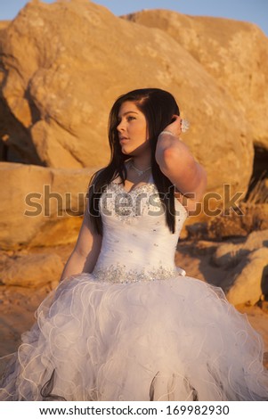 a woman in her formal dress standing by rocks with her hand in her hair.