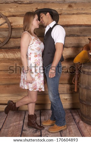 A cowboy is about to kiss his cowgirl in front of a wooden wall.