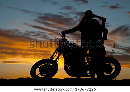 A silhouette of a man and woman next to a motorcycle holding each other.