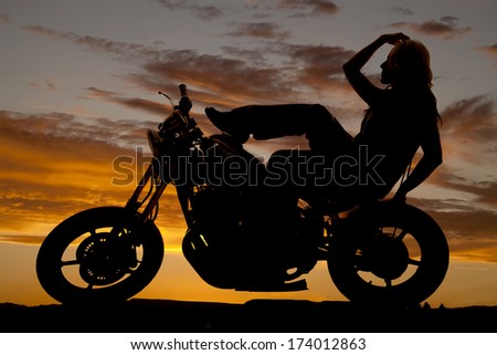 A silhouette of a woman sitting back on a motorcycle.