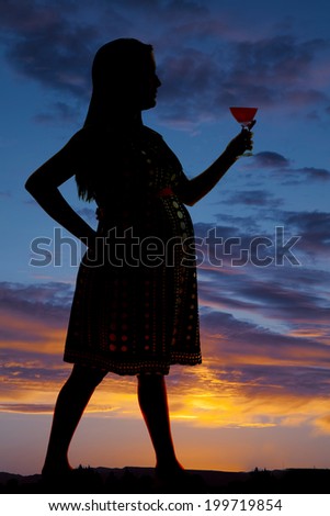 A silhouette of a woman standing holding a drink in her hand.