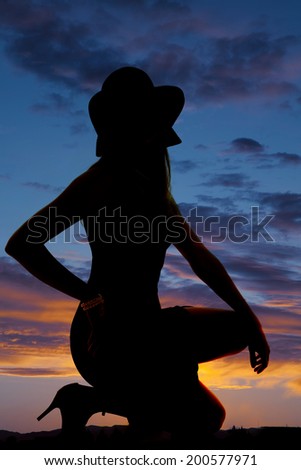 A silhouette of a woman kneeling on the ground wearing a hat.