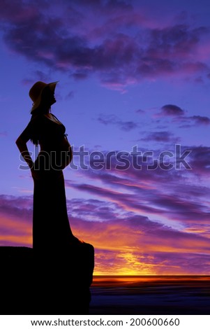 A silhouette of a woman who is pregnant standing on a ledge.