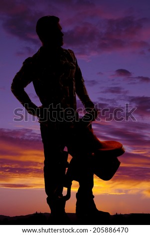 A silhouette of a cowboy holding on to his saddle looking to the side.