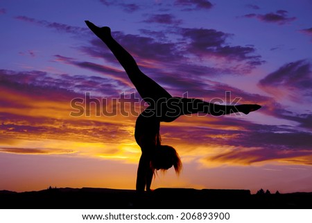 A silhouette of a woman doing a handstand split in the outdoors.