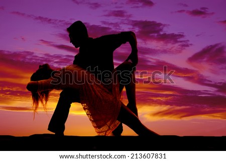 A silhouette of a man and woman dancing she is leaning back over his knee.