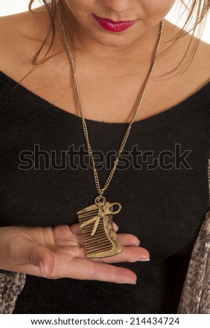 A woman holding on to a comb and scissor charm necklace.