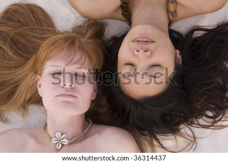 Two women laying with their heads together in the sand.