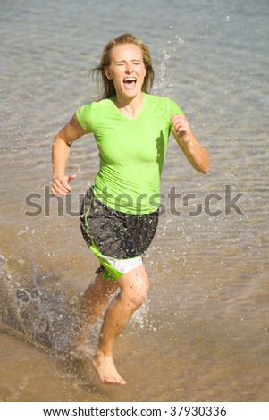 A woman running in the water splashing and having a lot of fun getting wet.