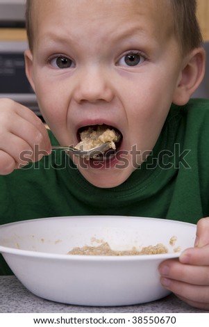 Young boy eating oatmeal for breakfast taking a big bite