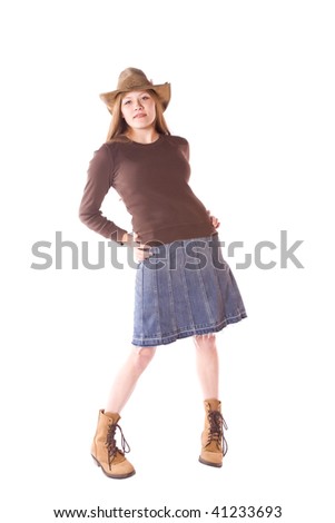 A woman standing in a denim skirt with a hat on and with a small smile on her face.