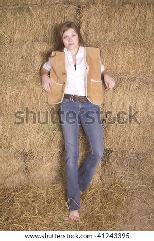 A woman standing in her bare feet by a hay stack with a serious look on her face.