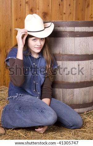 A woman tipping her white hat while kneeling by a wooden barel with a small smile on her face.
