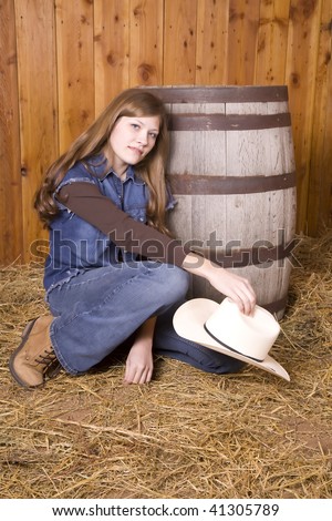 A woman kneeling down by a barrel with a sad look on her face holding a white hat.